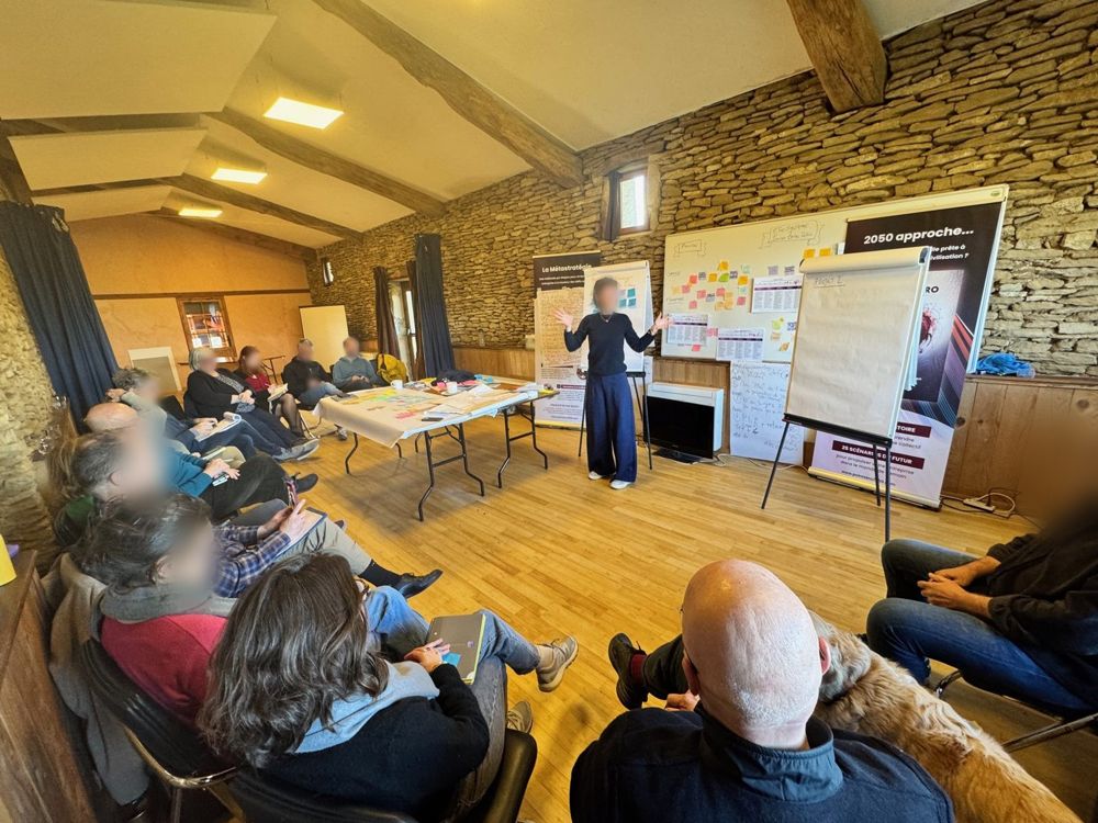 Une intervenante face au groupe assis en arc de cercle, paperboards et tables de travail